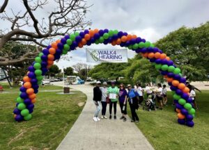 People standing at the Walk4Hearing balloon arch display