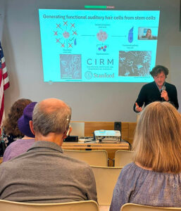Noah Linder speaking in front of the group and on Zoom
